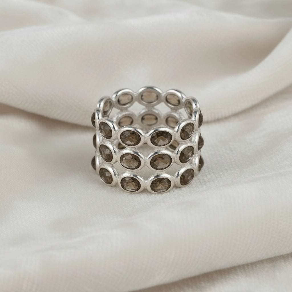 Horizontal close up shot of a wide sterling silver smoky quartz ring on a white velvet background with three rows of oval stones