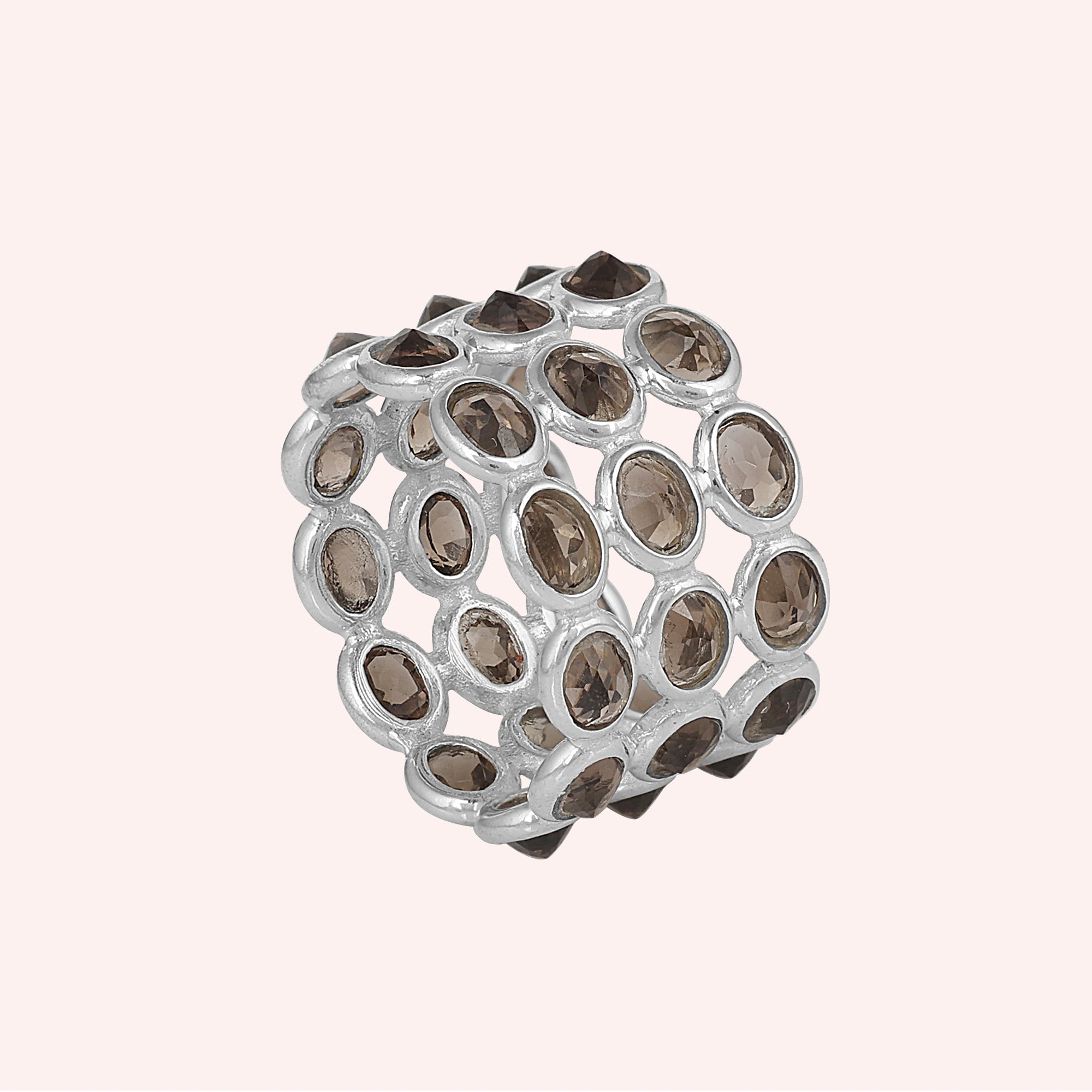 Angled shot of a wide sterling silver smoky quartz ring on a light pink background with three rows of oval smoky quartz stones