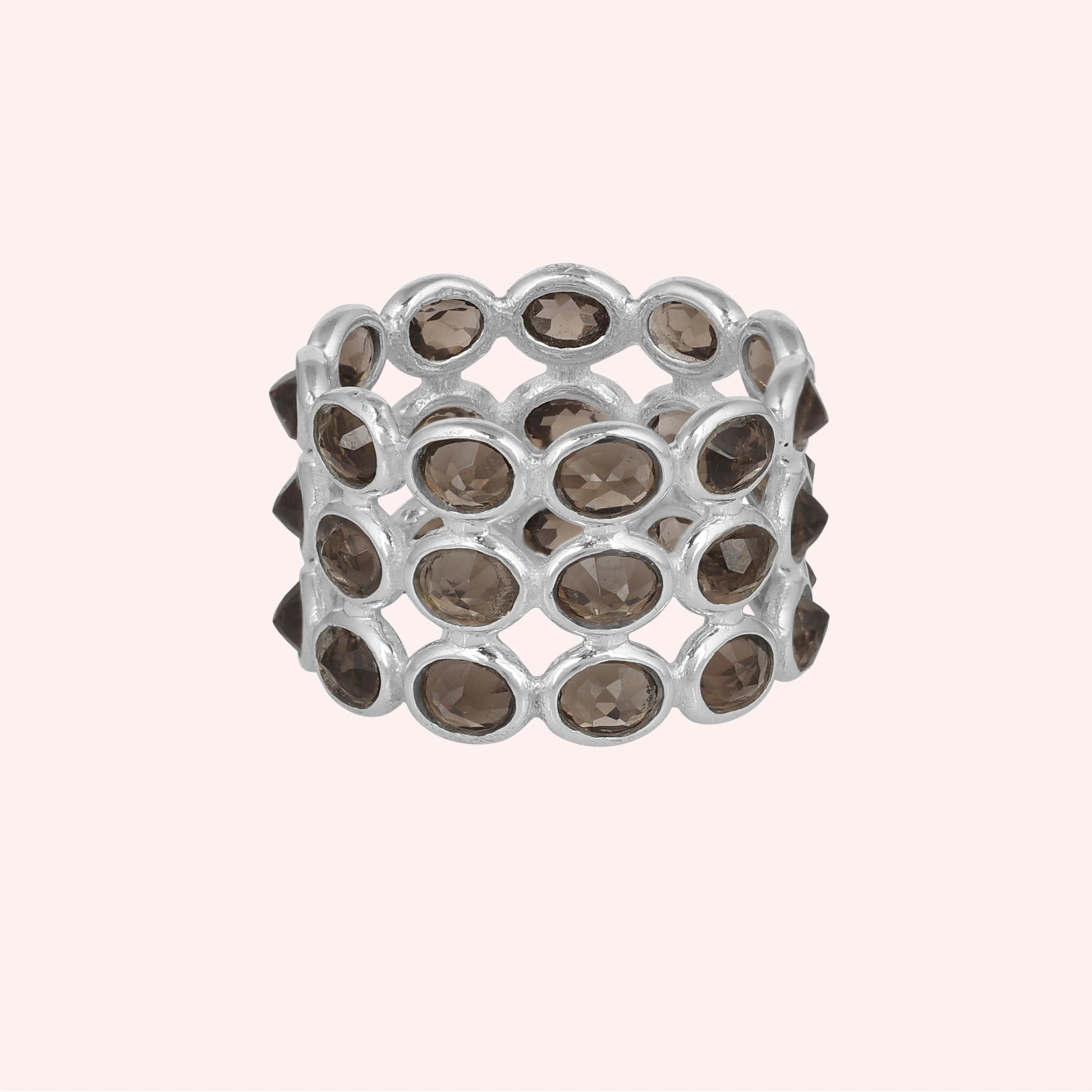 Horizontal shot of a wide sterling silver smoky quartz ring on a light pink background with three rows of oval stones