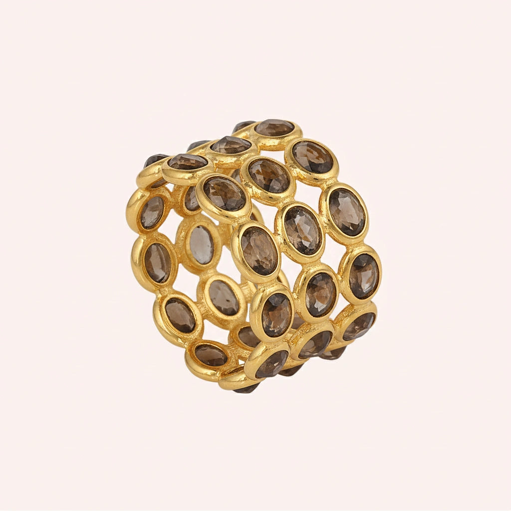 Angled shot of a wide gold-plated sterling silver smoky quartz ring on a light pink background with three rows of oval stones