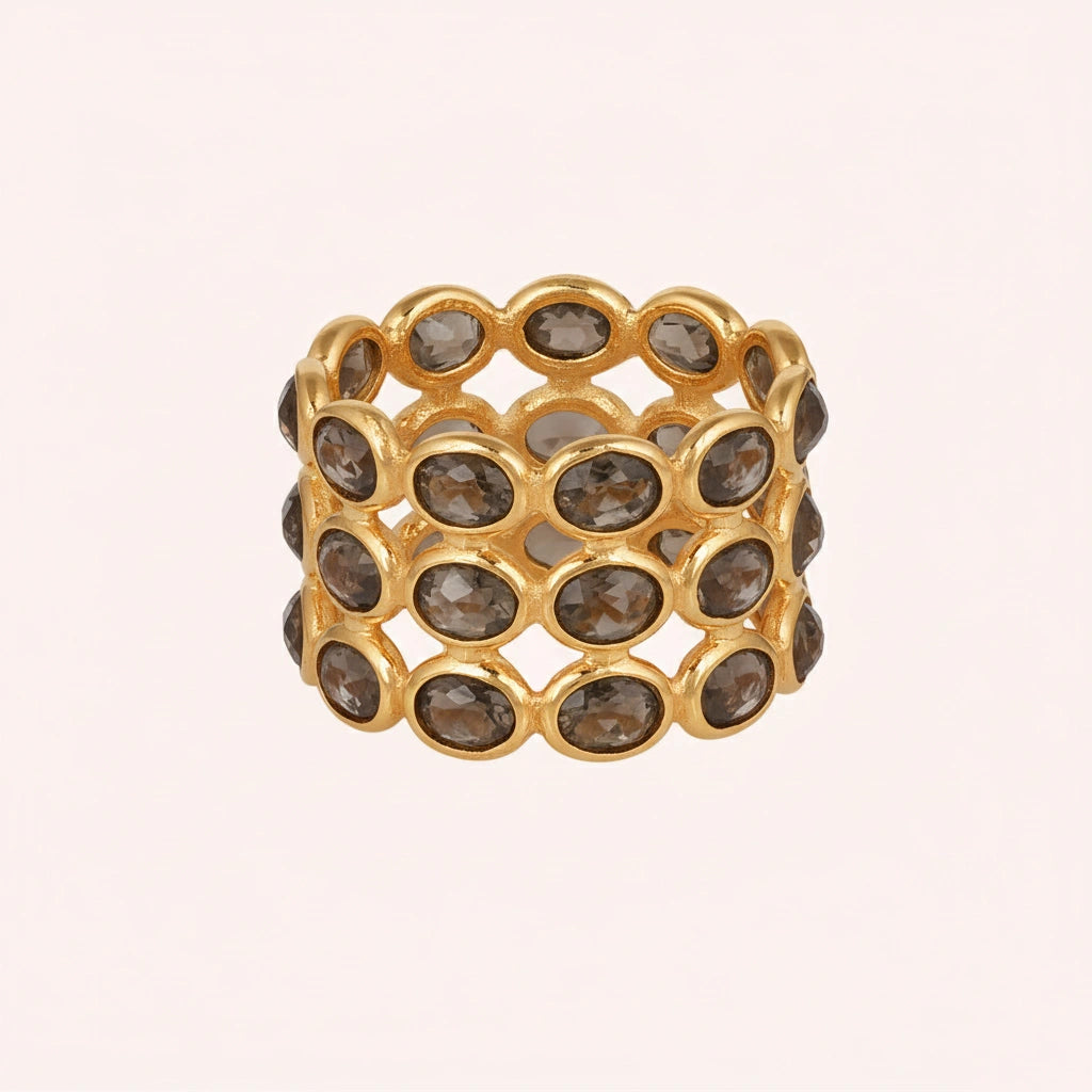 Horizontal shot of a wide gold-plated sterling silver smoky quartz ring on a light pink background with three rows of oval stones