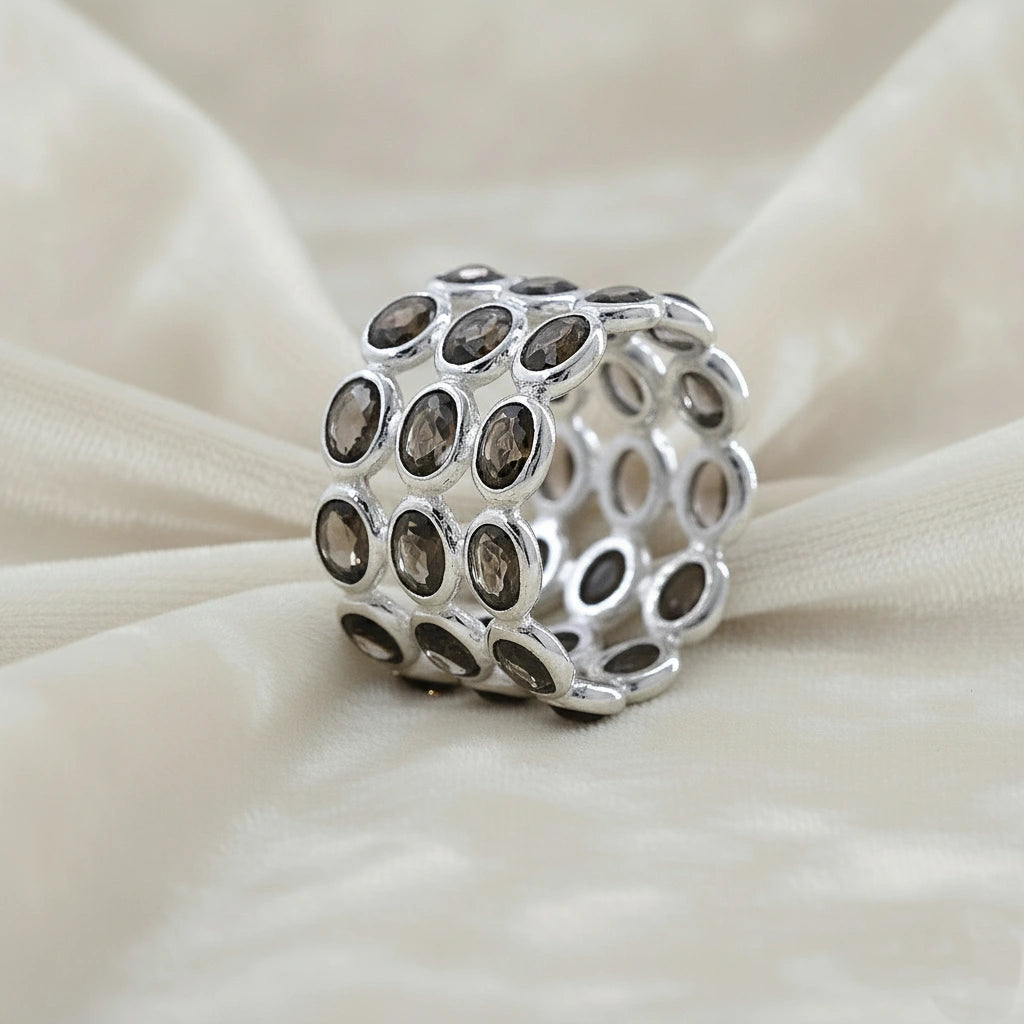 Angled close up shot of a wide sterling silver smoky quartz ring on a white velvet background with three rows of oval stones