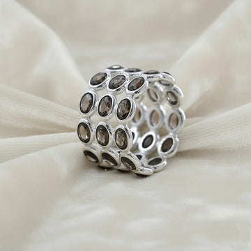 Angled close up shot of a wide sterling silver smoky quartz ring on a white velvet background with three rows of oval stones