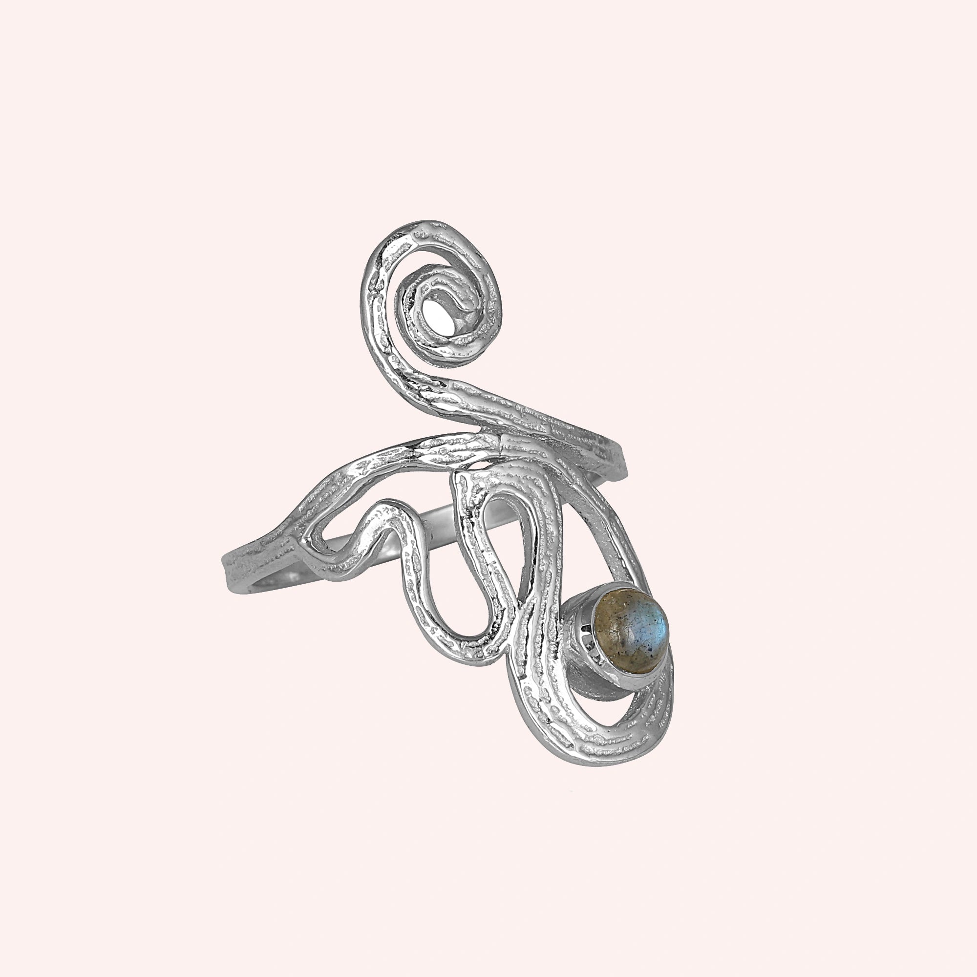 A silver solar ring on a pink background shown from a side angle with a round labradorite stone and a dainty crystal ring