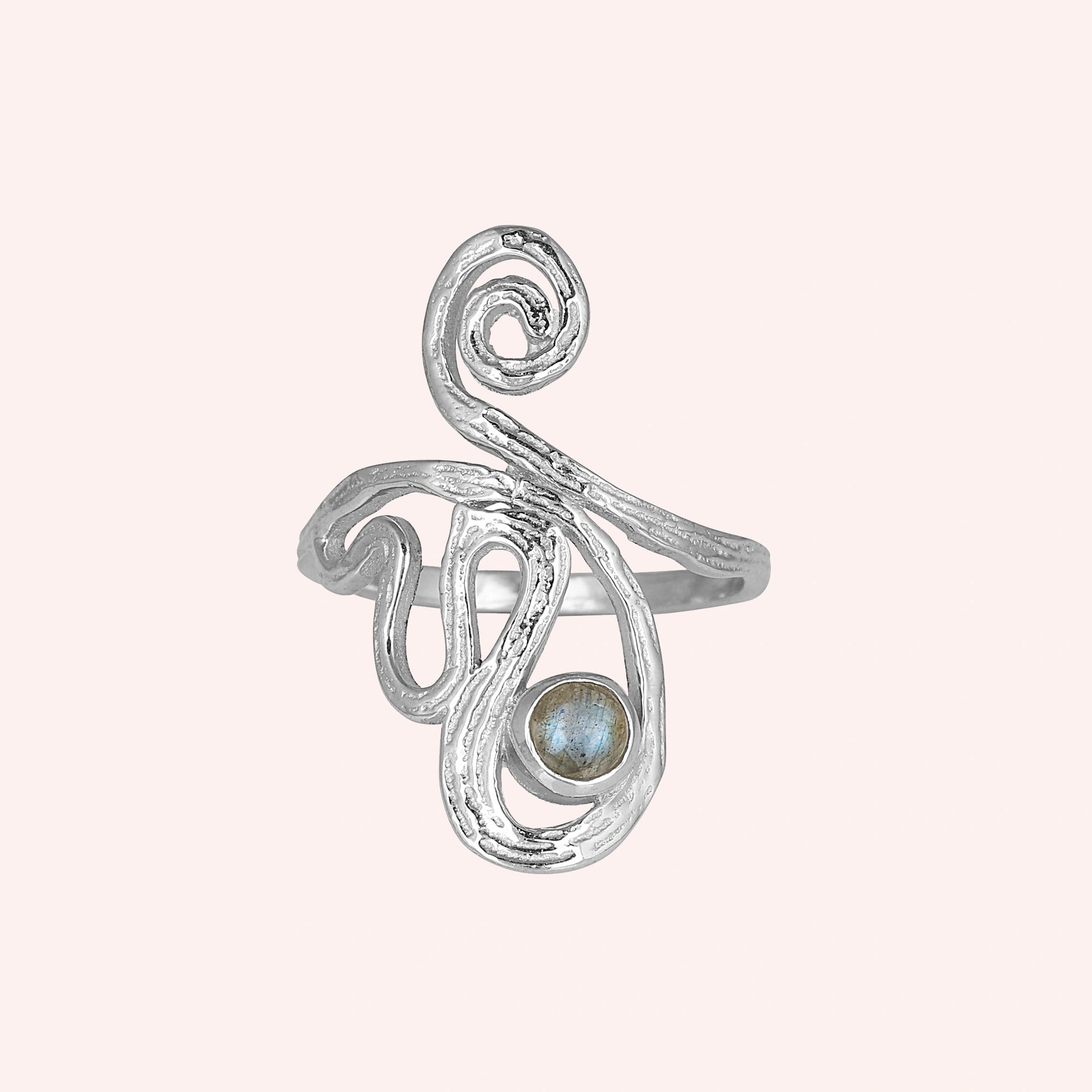 A silver solar ring on a pink background shown from a front angle featuring a round labradorite stone and a dainty crystal ring