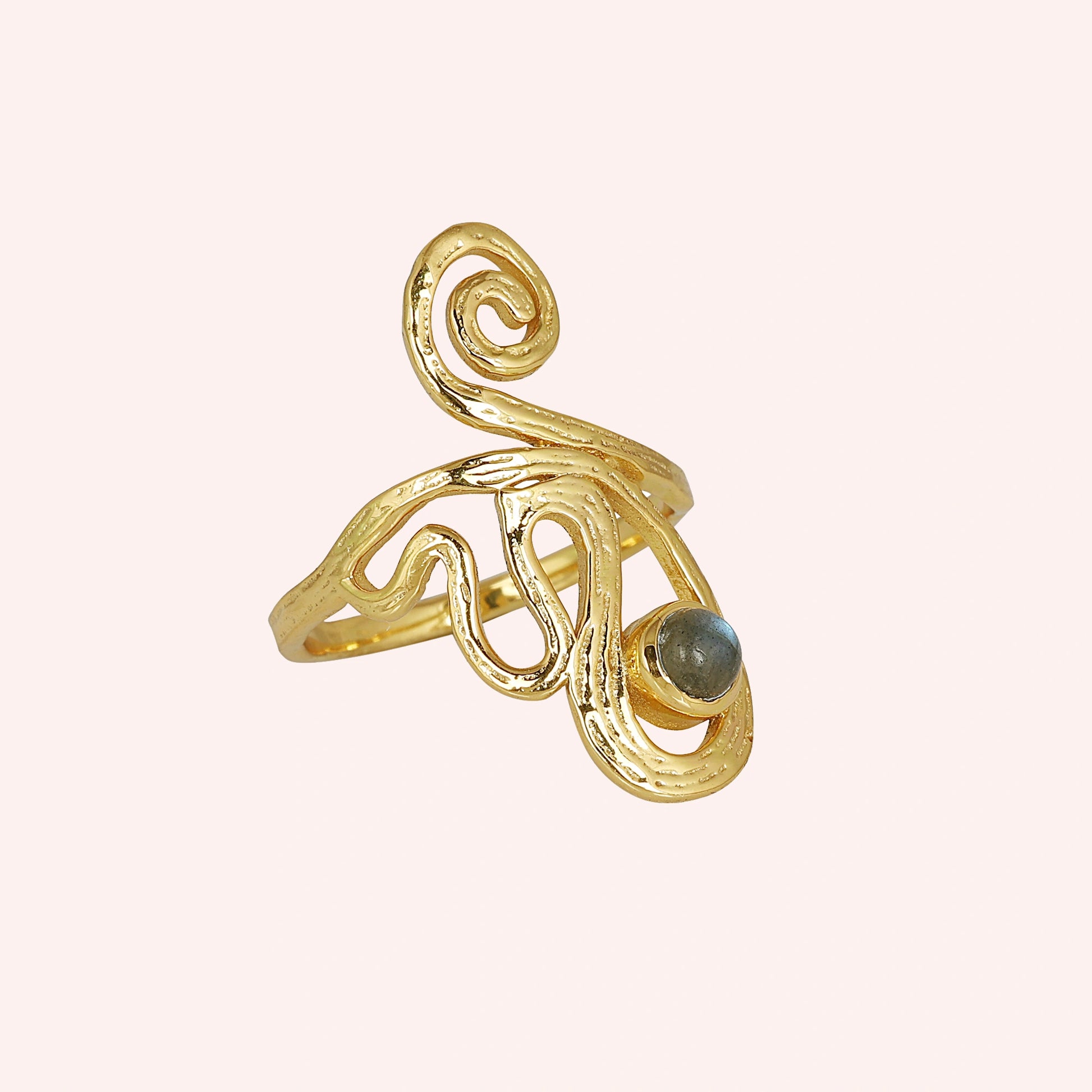 A gold plated solar ring on a pink background shown from a side angle with a round stone and a dainty crystal ring band