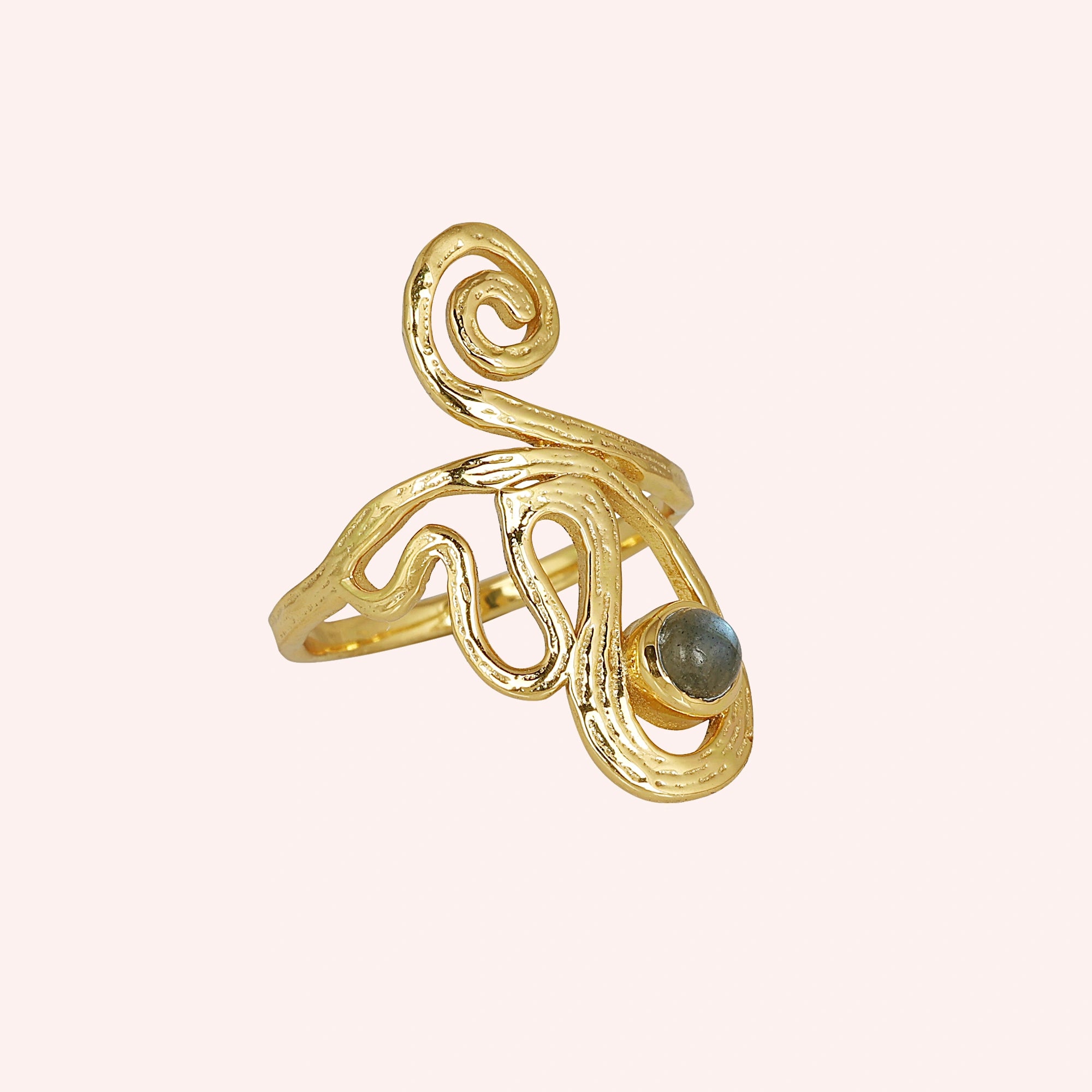 A gold plated solar ring on a pink background shown from a side angle with a round stone and a dainty crystal ring band