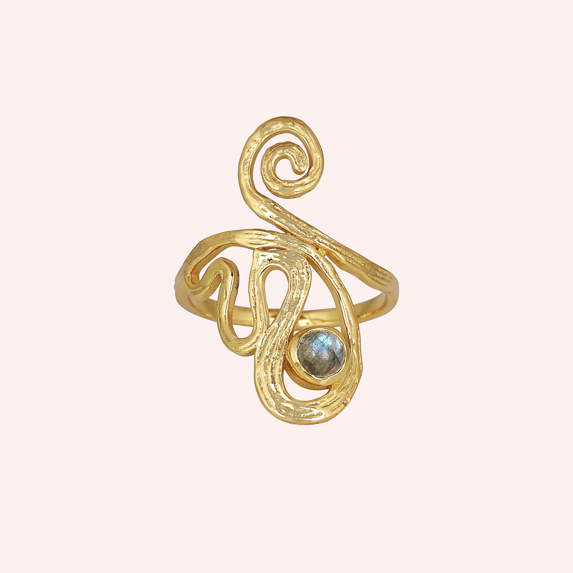 A gold plated solar ring on a pink background shown from a front angle with a round stone and a dainty crystal ring band