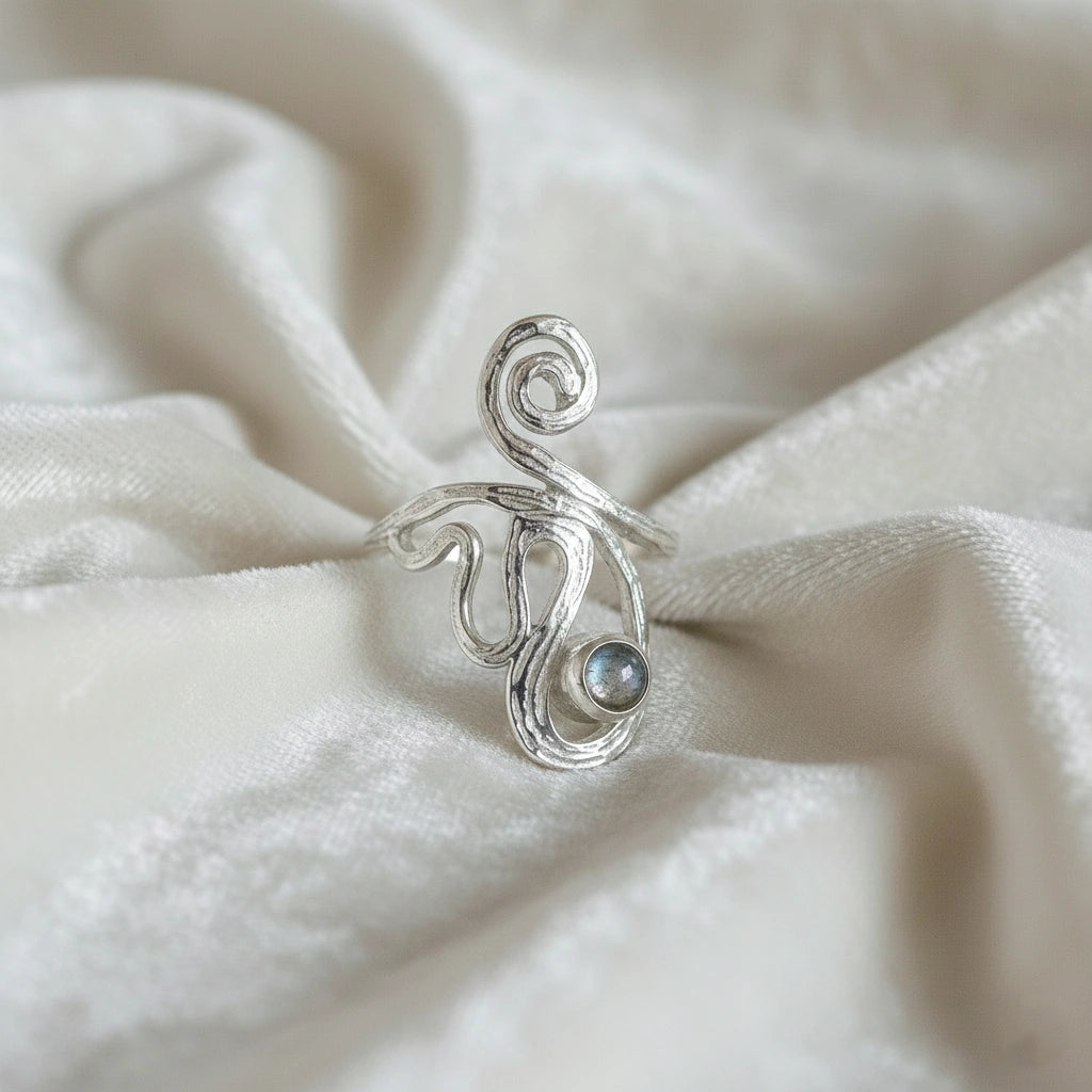 solar ring crystal ring shown at front angled view featuring spiral silver design with gemstone on soft white fabric background