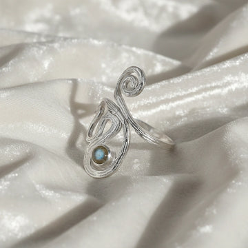 solar ring crystal ring shown at a side angled view featuring spiral silver design with gemstone on soft white fabric background