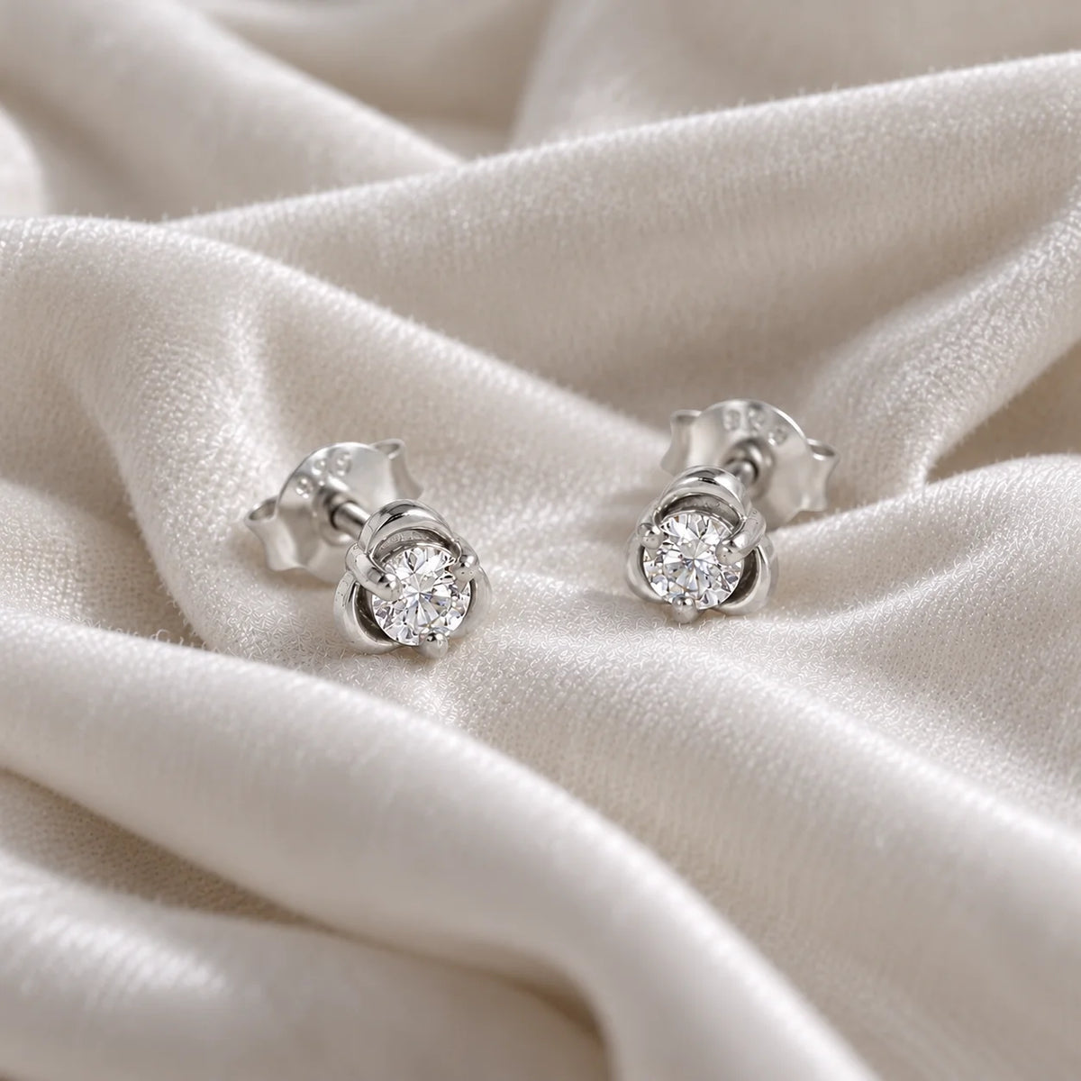 Solitaire_earrings_in_sterling_silver_with_a_round_lab_grown_diamond_at_front_angle_view_on_soft_fabric_background