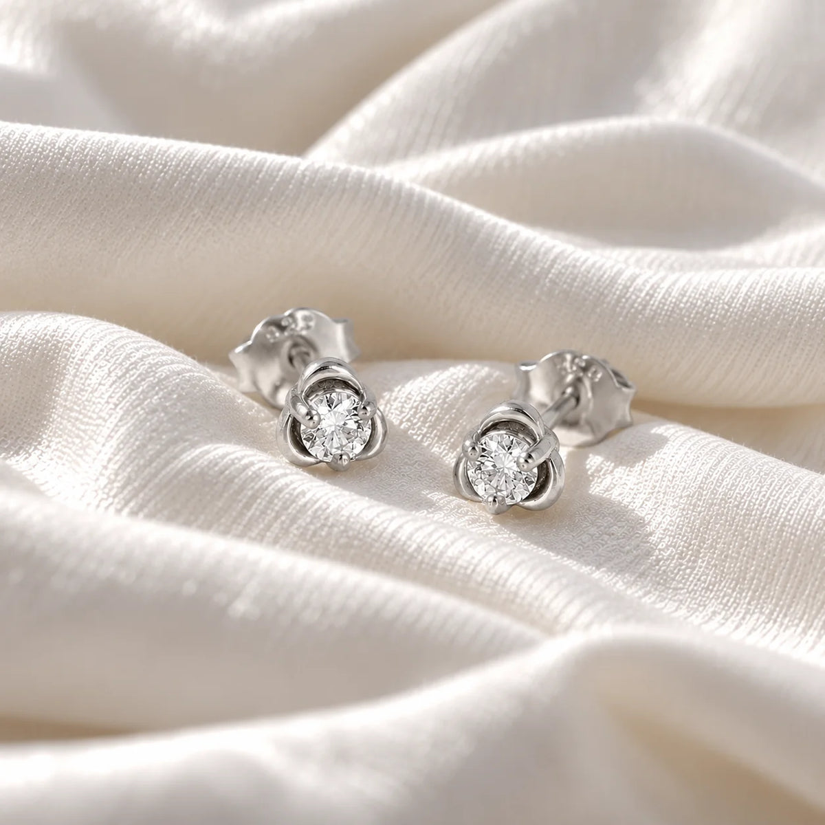 Solitaire_earrings_in_sterling_silver_in_a_floral_design_at_front_angle_view_on_soft_fabric_background