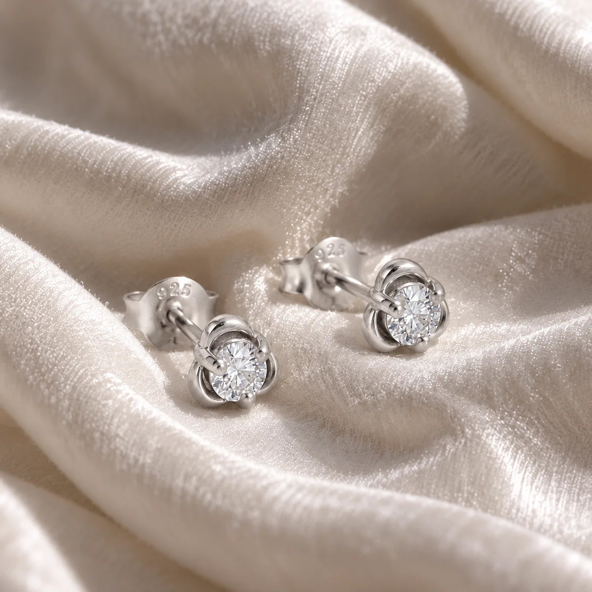 Solitaire_earrings_in_sterling_silver_with_a_round_lab_grown_diamond_at_side_angle_view_on_soft_fabric_background