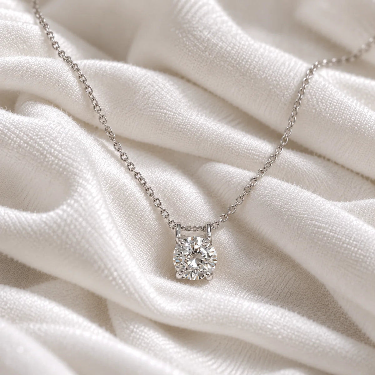 Solitaire_necklace_in_sterling_silver_with_a_round_lab_grown_diamond_at_front_angle_view_on_soft_fabric_background