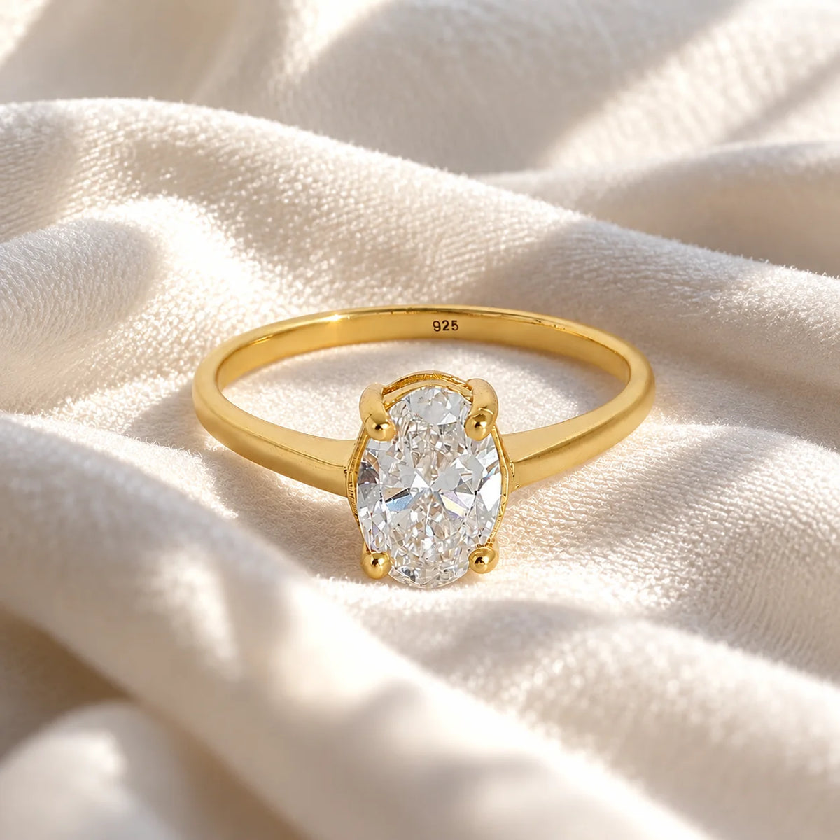 Solitaire_ring_in_gold_plated_silver_with_an_oval_lab_grown_diamond_at_front_angle_view_on_soft_fabric_background