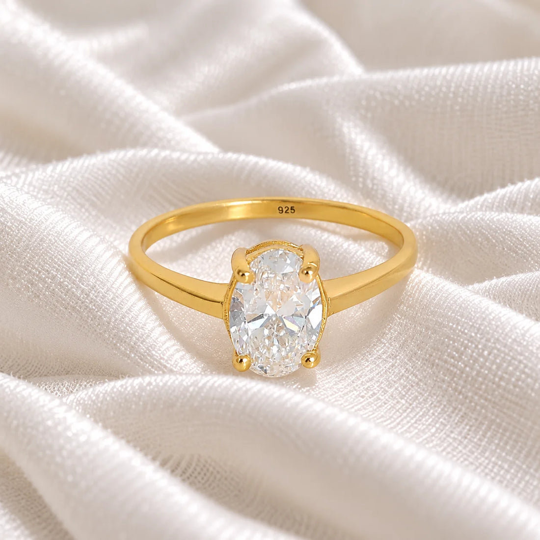 Solitaire_ring_in_gold_plated_silver_with_an_oval_CZ_stone_at_front_angle_view_on_soft_fabric_background