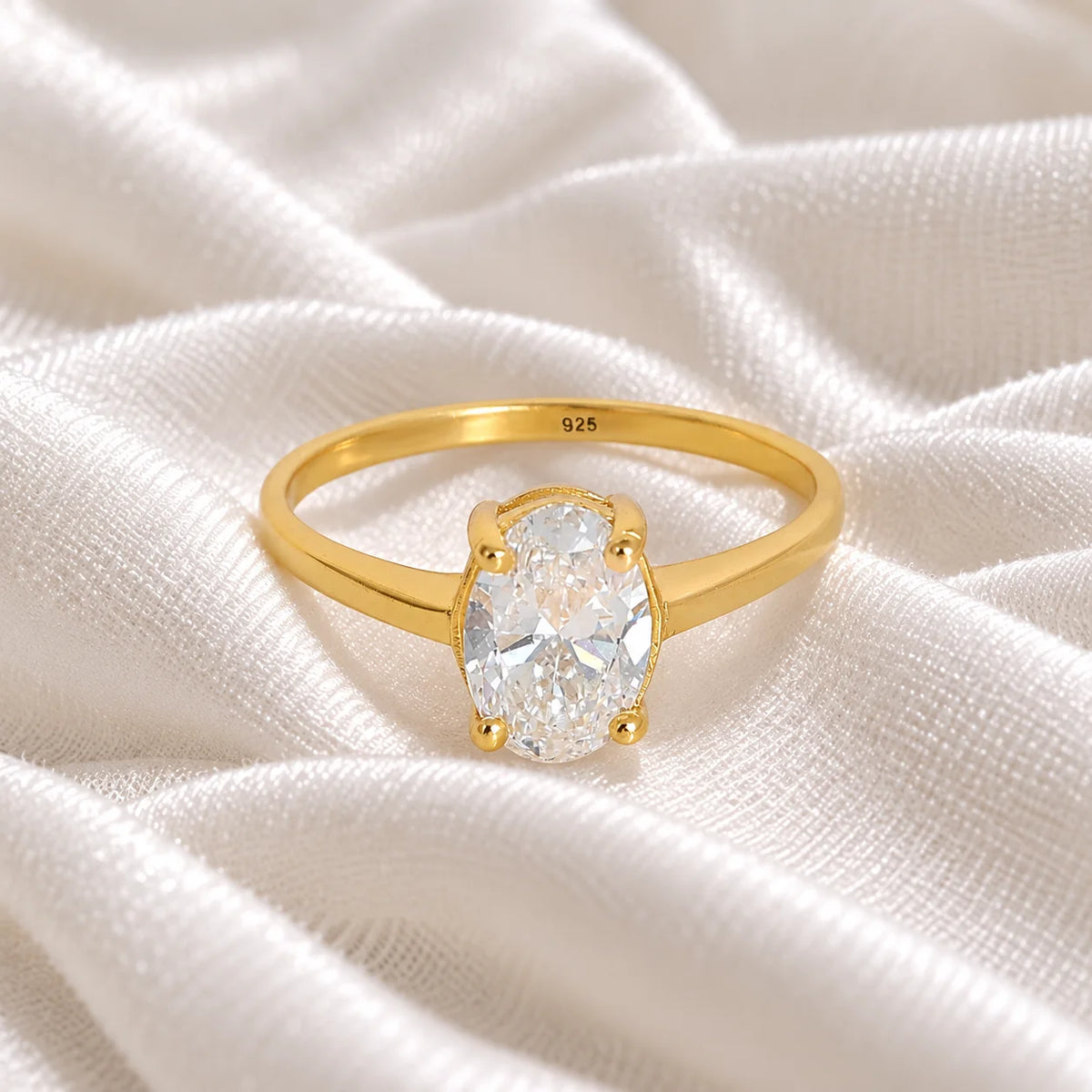 Solitaire_ring_in_gold_plated_silver_with_an_oval_CZ_stone_at_front_angle_view_on_soft_fabric_background