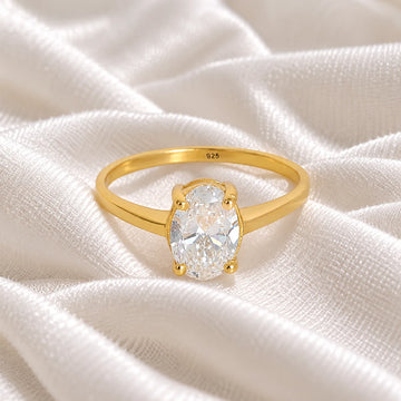 Solitaire_ring_in_gold_plated_silver_with_an_oval_CZ_stone_at_front_angle_view_on_soft_fabric_background