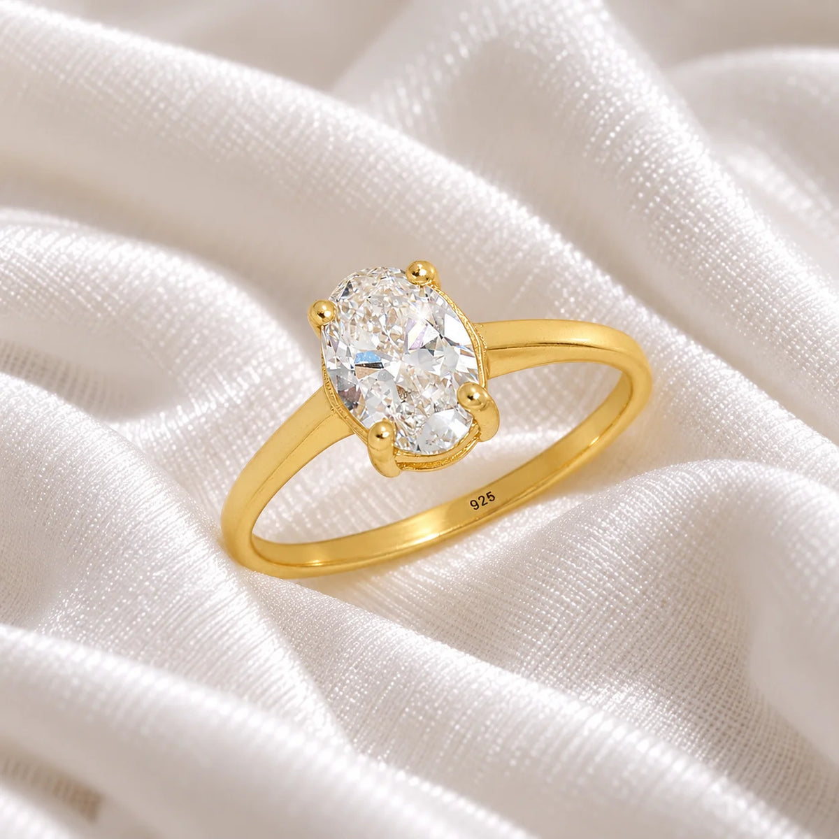 Solitaire_ring_in_gold_plated_silver_with_an_oval_CZ_stone_at_side_angle_view_on_soft_fabric_background