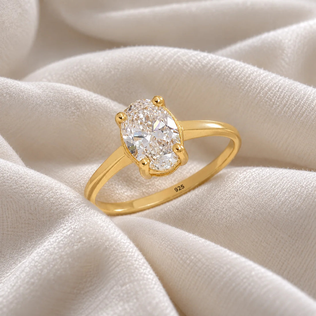 Solitaire_ring_in_gold_plated_silver_with_an_oval_lab_grown_diamond_at_slightly_angle_view_on_soft_fabric_background