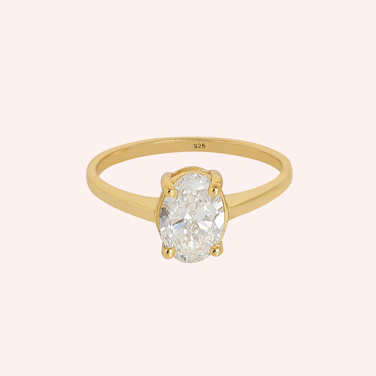 Solitaire_ring_in_gold_plated_silver_with_an_oval_CZ_stone_at_front_angle_view_on_solid_pink_background