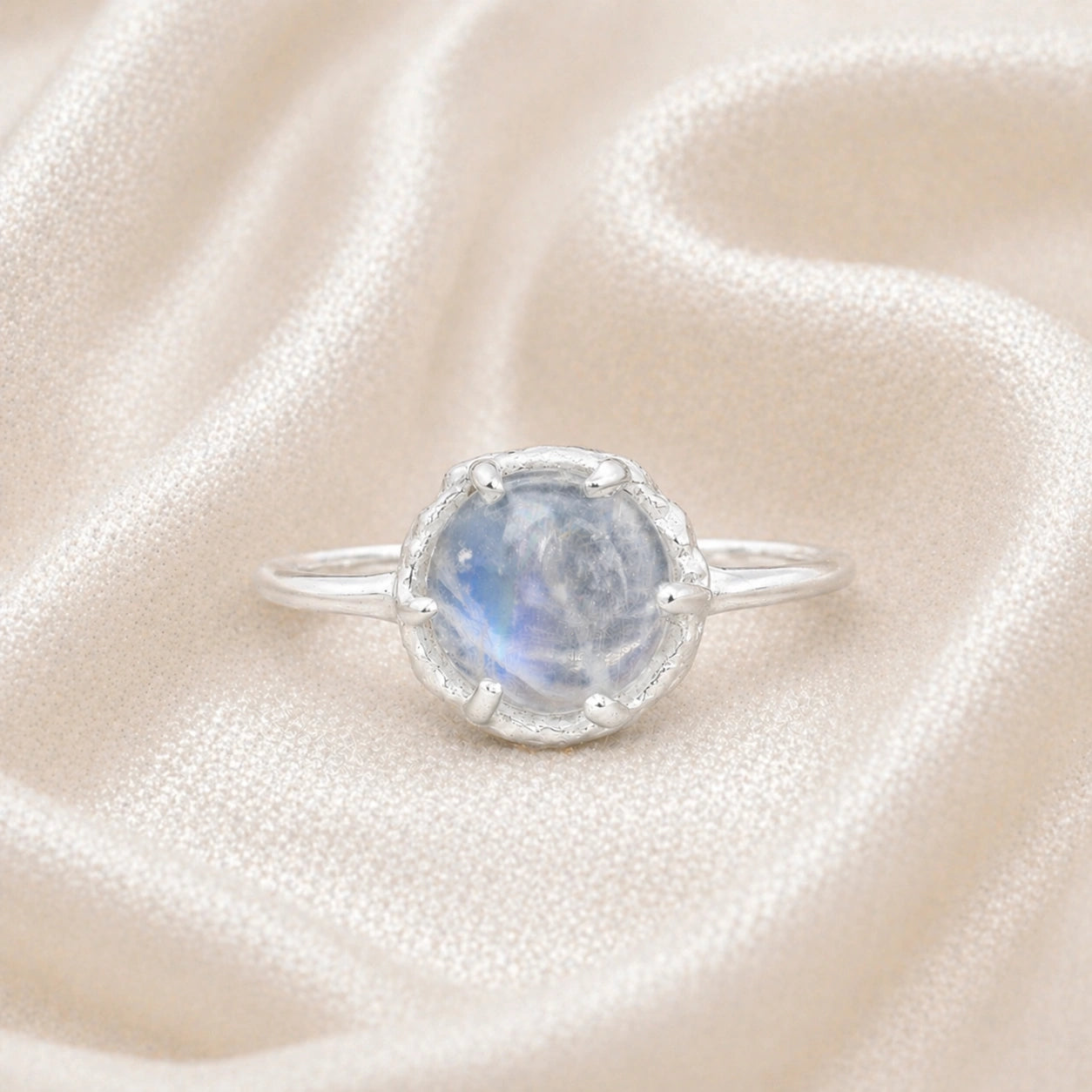 Solitaire_ring_in_sterling_ring_with_round_moonstone_shown_in_front_angle_view_on_soft_fabric_background