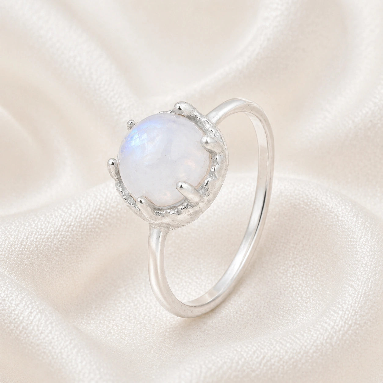 Solitaire_ring_in_sterling_ring_with_round_moonstone_shown_in_slightly_angled_view_on_soft_fabric_background