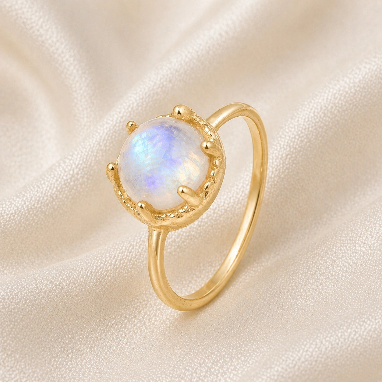 Solitaire_ring_in_gold_plated_ring_with_round_moonstone_shown_in_slightly_angled_view_on_soft_fabric_background
