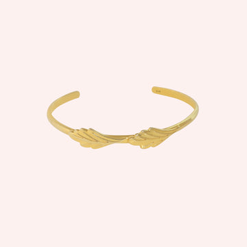 Stacking_bracelet_in_gold_plated_silver_with_a_leaf_design_band_at_front_angle_view_on_solid_pink_background