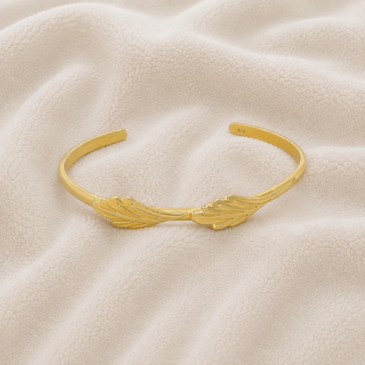 Stacking_bracelet_in_gold_plated_silver_with_a_leaf_design_band_at_front_angle_view_on_soft_fabric_background