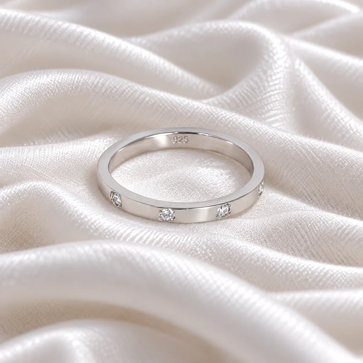 Stacking_ring_in_sterling_silver_with_a_round_CZ_stones_at_front_angle_view_on_soft_fabric_background