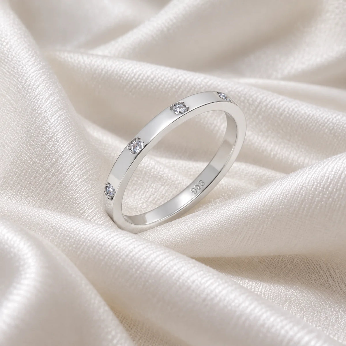 Stacking_ring_in_sterling_silver_with_a_round_CZ_stones_at_side_angle_view_on_soft_fabric_background