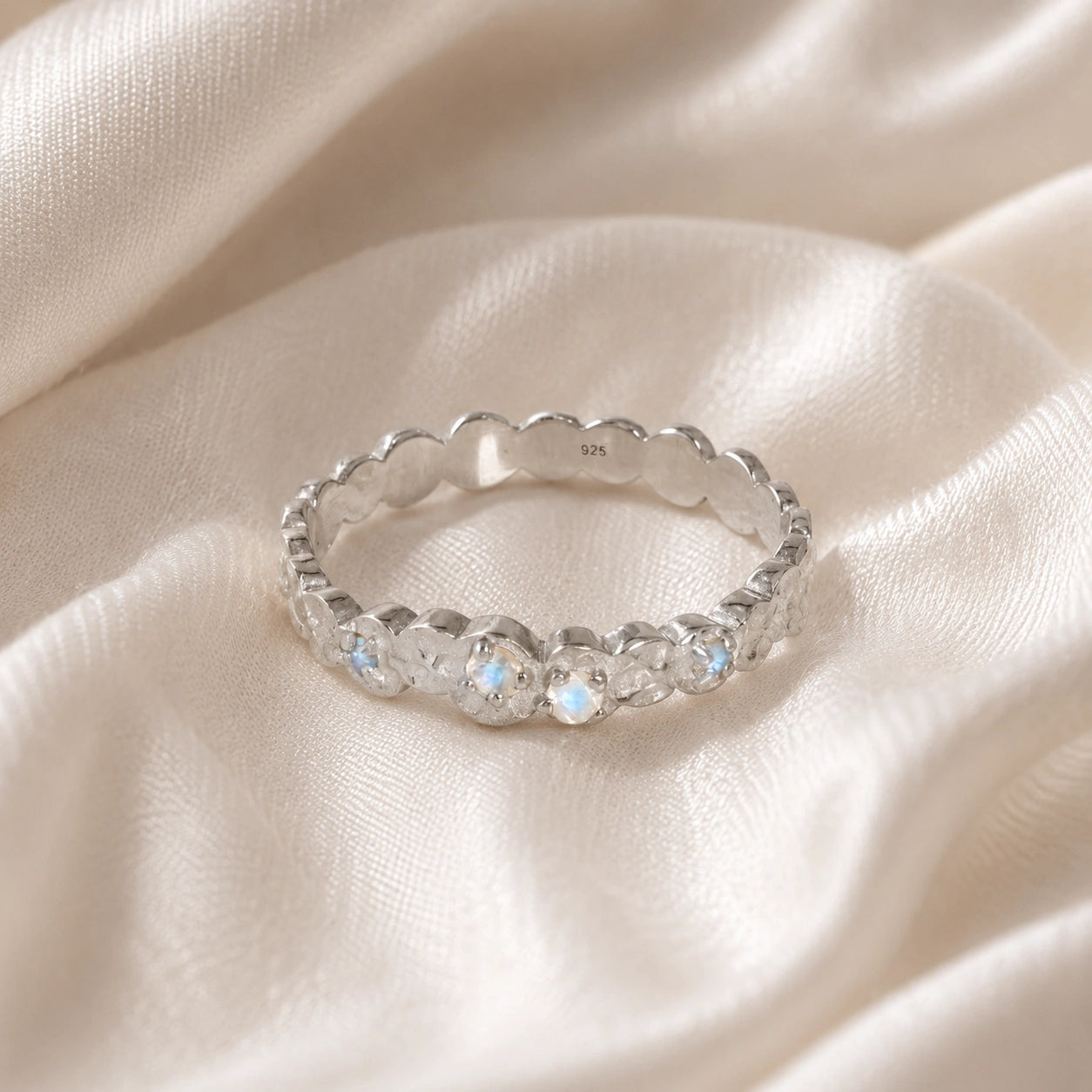 Stacking_ring_in_sterling_silver_textured_band_with_moonstones_in_front_angled_view_on_soft_fabric_background