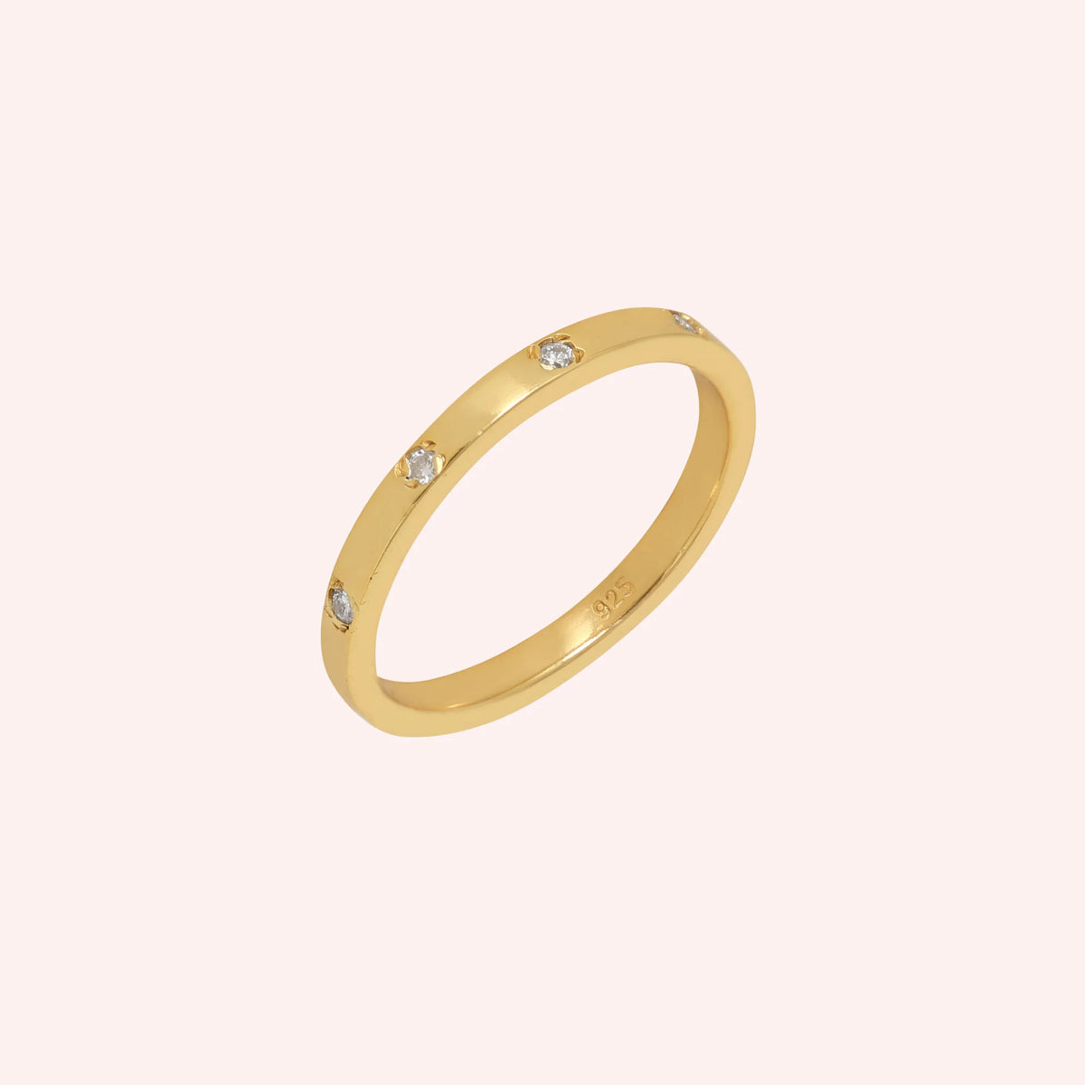 Stacking_ring_in_gold_plated_silver_with_a_round_CZ_stones_at_side_angle_view_on_solid_pink_background