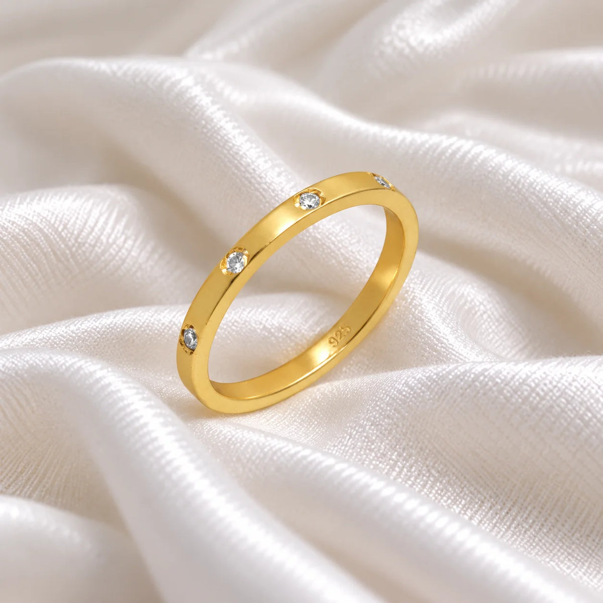 Stacking_ring_in_gold_plated_silver_with_a_round_CZ_stones_at_side_angle_view_on_soft_fabric_background