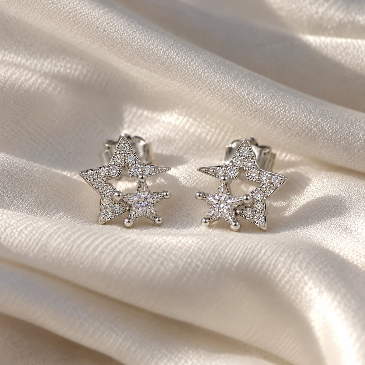 Star_earrings_in_sterling_silver_with_CZ_stones_at_front_angle_view_on_soft_fabric_background