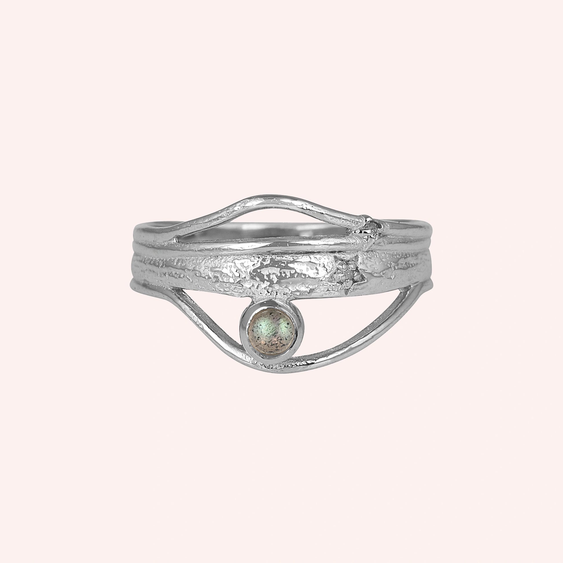 A silver wave ring statement ring with a textured band and round labradorite stone at a front angle over a pink background