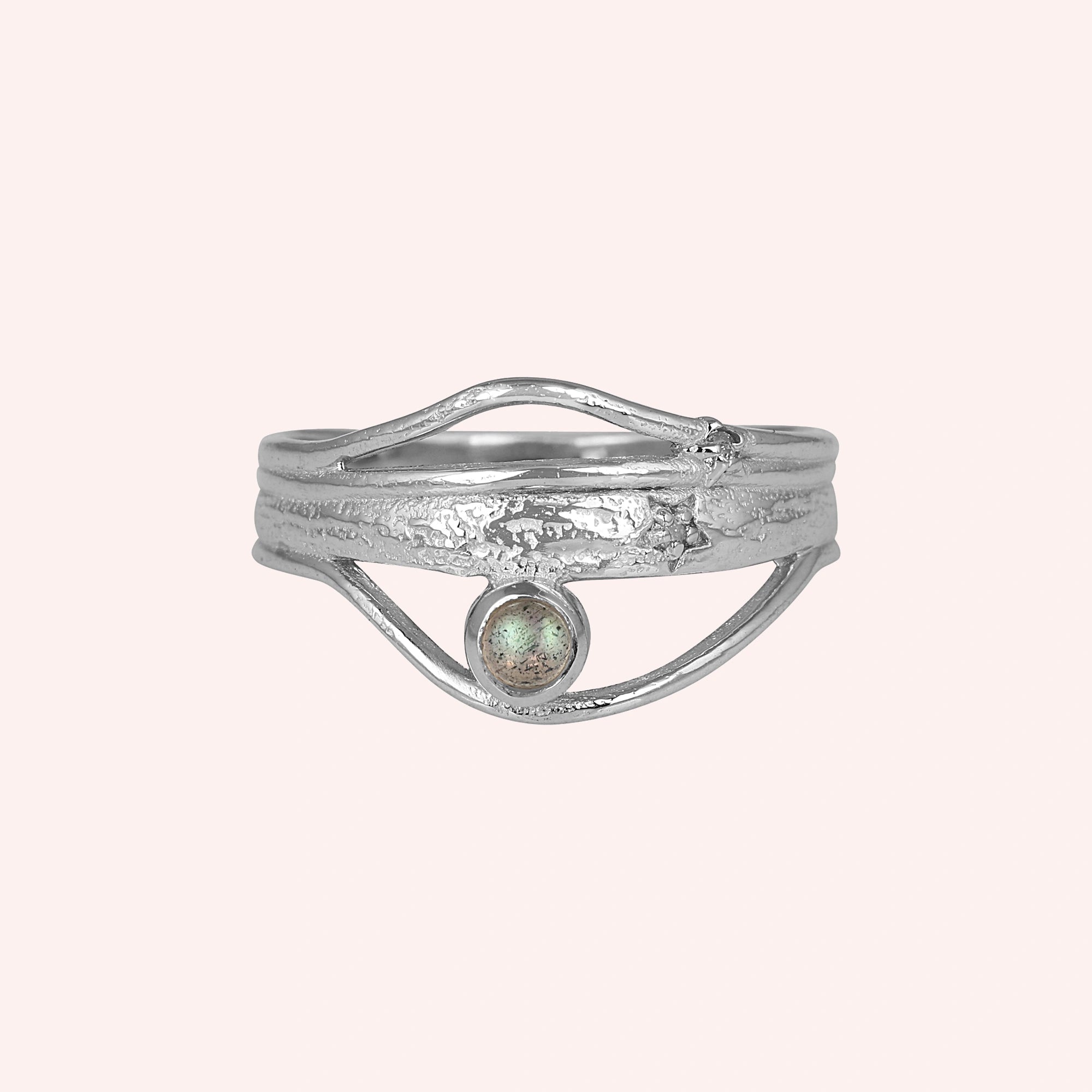 A silver wave ring statement ring with a textured band and round labradorite stone at a front angle over a pink background