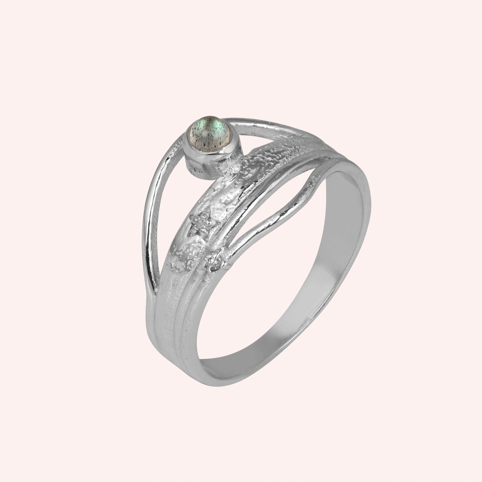 A silver wave ring on a light pink background shown at a side angle with a labradorite stone and textured statement ring band