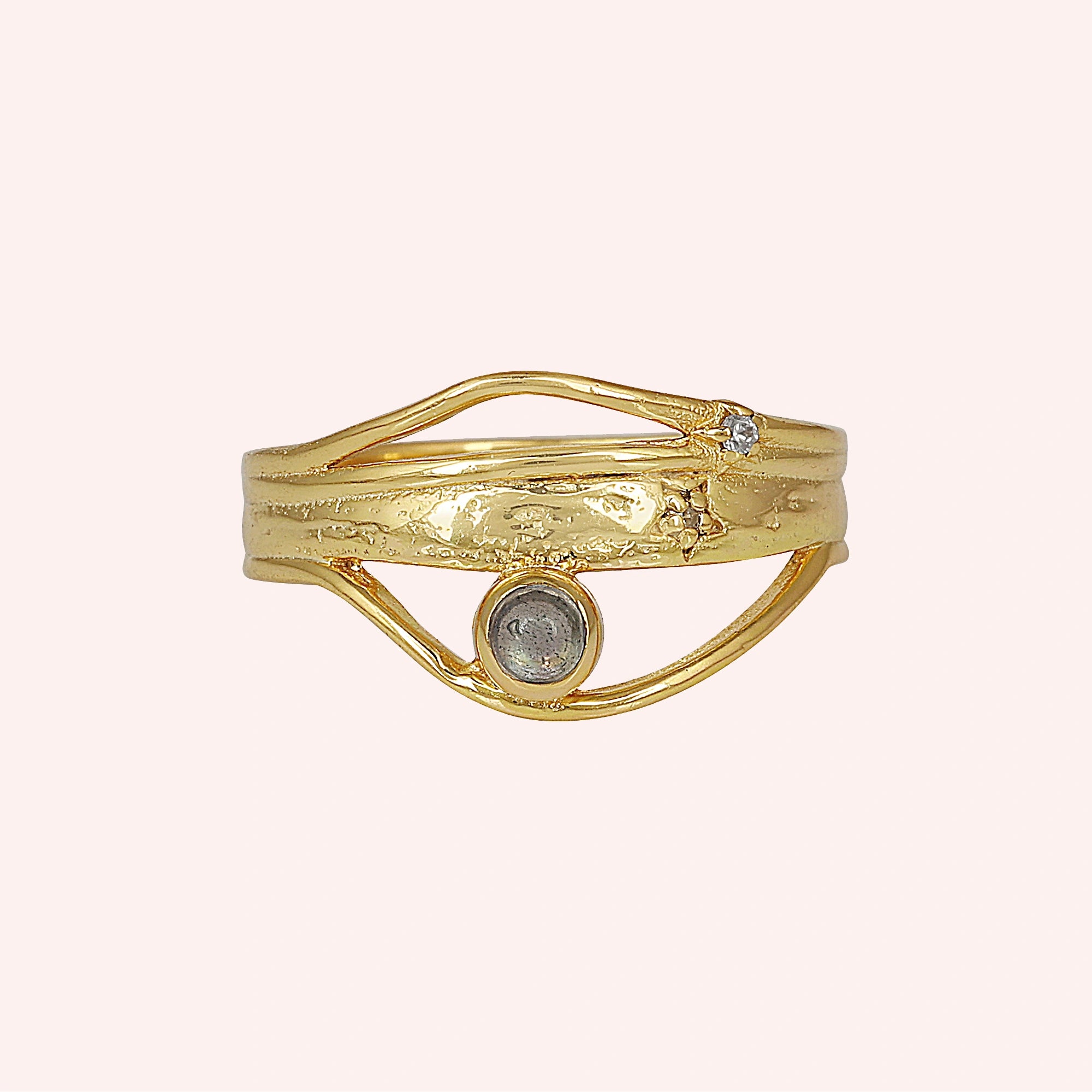 A gold plated wave ring with a labradorite on a pink background shown from a front angle as a textured statement ring design