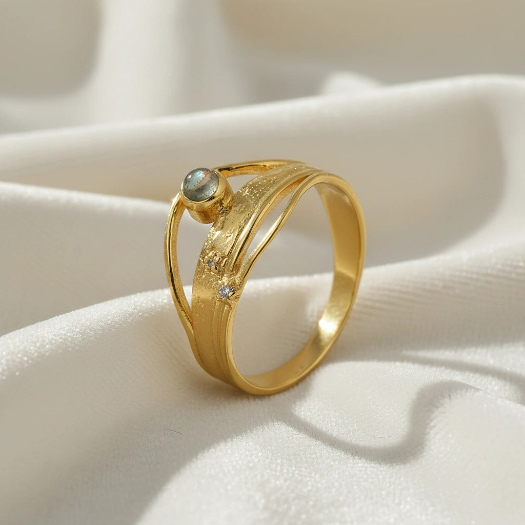 A gold plated wave ring with a labradorite on a white fabric shown from a side angle as a textured statement ring design