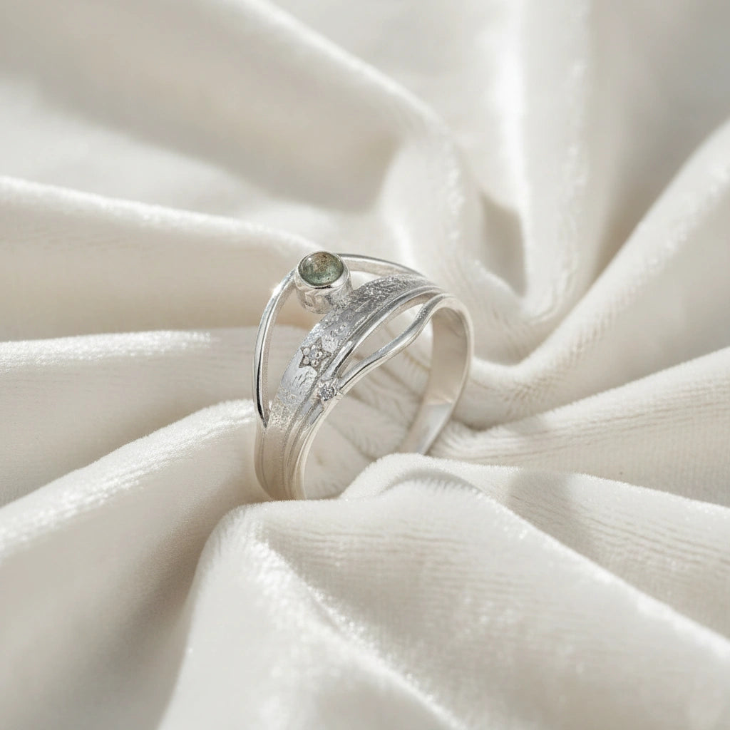A silver wave ring on a white fabric background shown at a side angle with a labradorite stone and textured statement ring band
