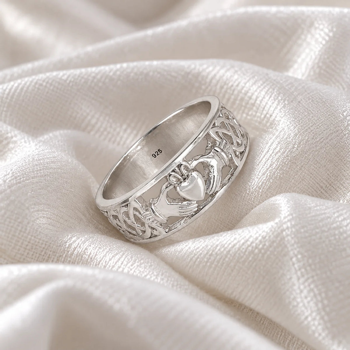 Statement_ring_in_sterling_silver_with_claddagh_design_band_at_side_angle_view_on_soft_fabric_background