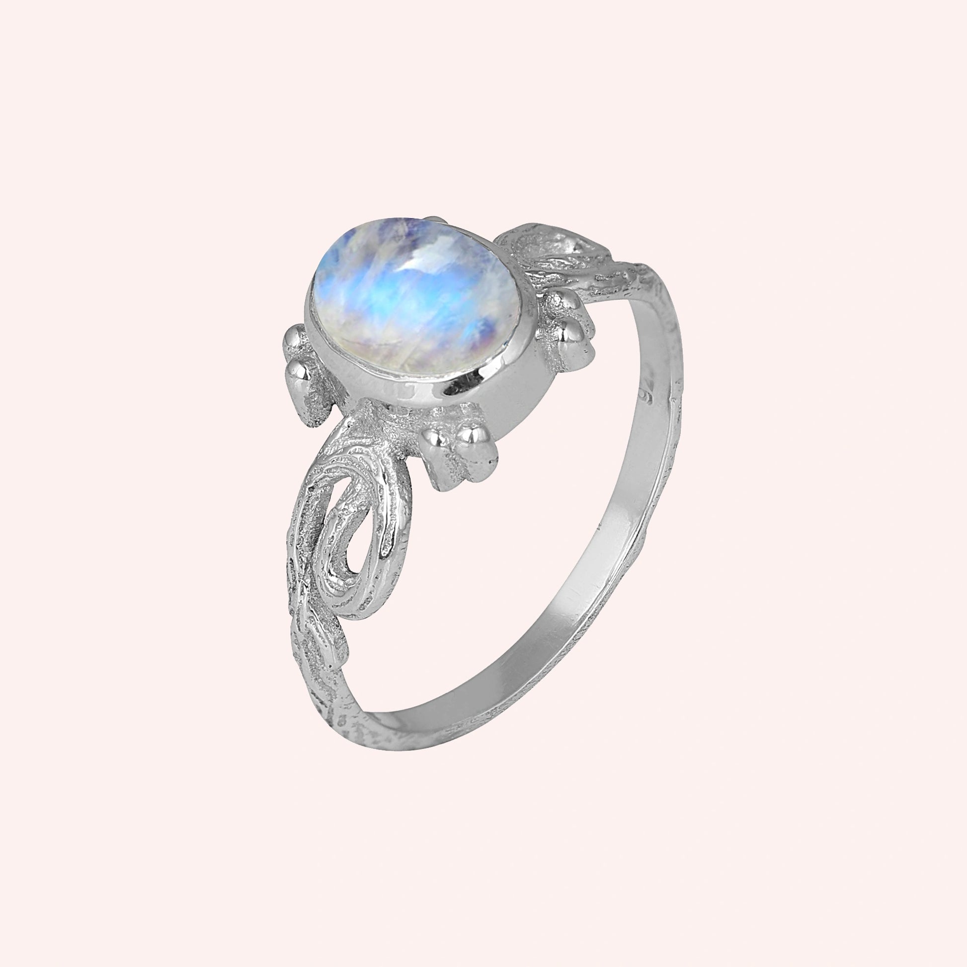 Statement_ring_sterling_silver_with_oval_moonstone_and_intricate_band_detail_slightly_tilted_view_on_solid_pink_background