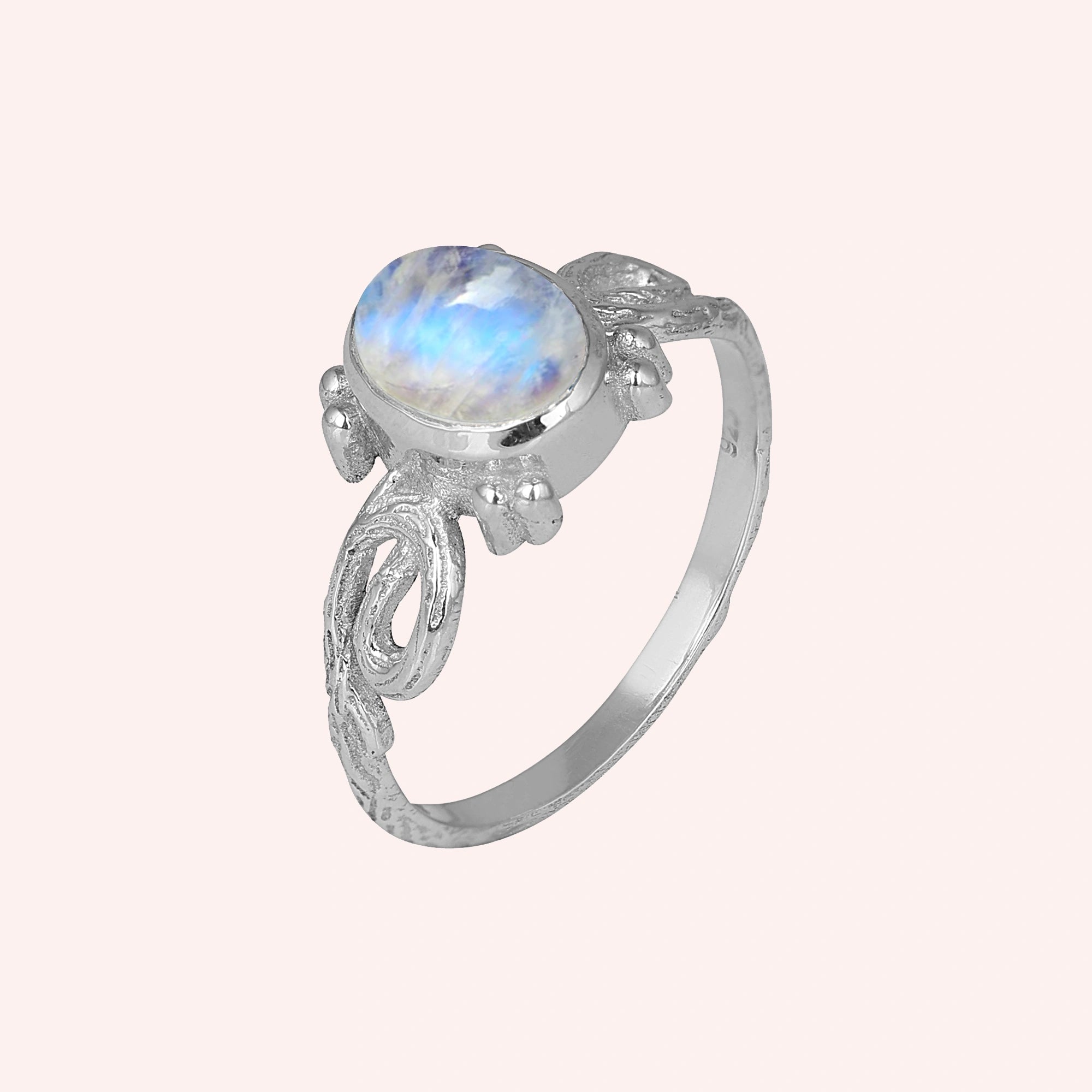 Statement_ring_sterling_silver_with_oval_moonstone_and_intricate_band_detail_slightly_tilted_view_on_solid_pink_background