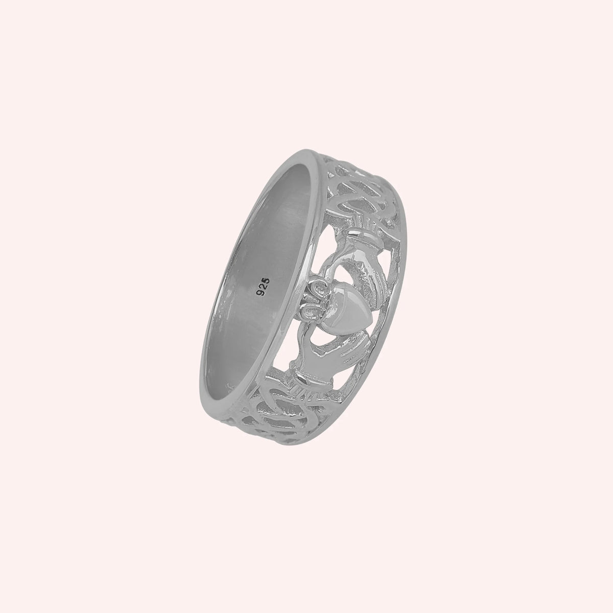 Statement_ring_in_sterling_silver_with_claddagh_design_band_at_side_angle_view_on_solid_pink_background