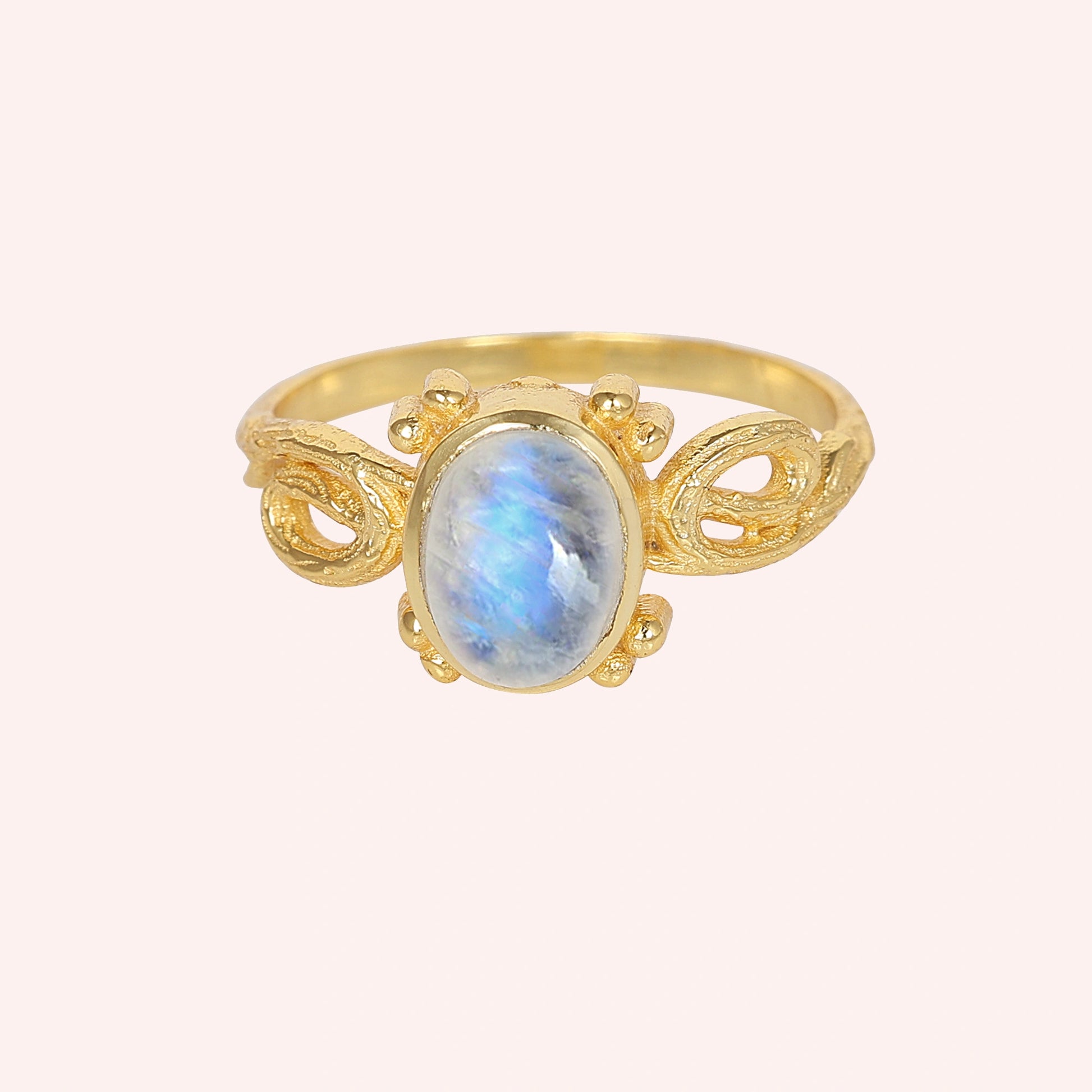 Statement_ring_gold_plated_silver_with_oval_moonstone_and_intricate_band_detail_front_angle_view_on_solid_pink_background