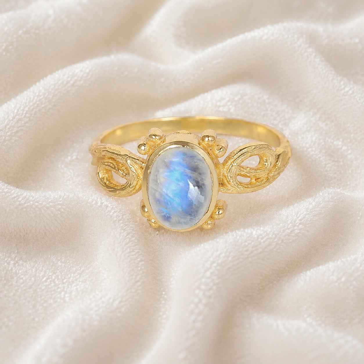 Statement_ring_gold_plated_silver_with_oval_moonstone_and_intricate_band_detail_front_angle_view_on_soft_fabric_background