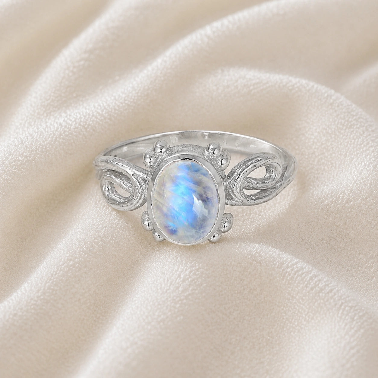 Statement_ring_sterling_silver_with_oval_moonstone_and_intricate_band_detail_front_angle_view_on_soft_fabric_background