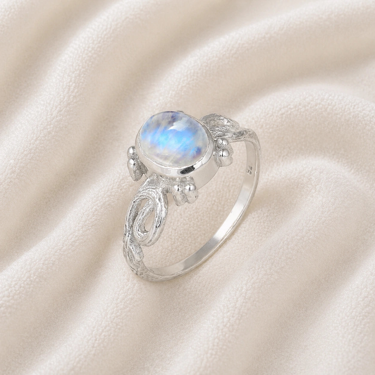 Statement_ring_sterling_silver_with_oval_moonstone_and_intricate_band_detail_slightly_tilted_view_on_soft_fabric_background